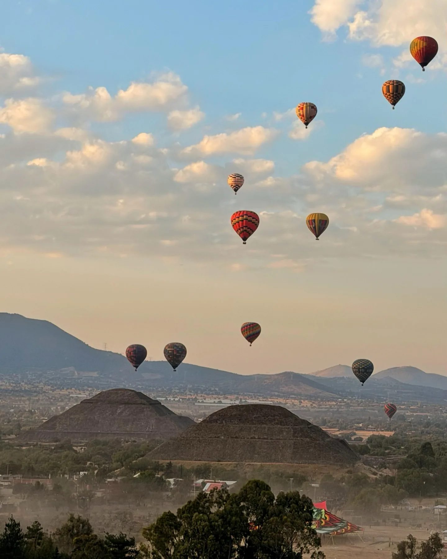 Hot air balloons drifting among the clouds above the Pyramid of the Sun and the Pyramid of the Moon at dawn