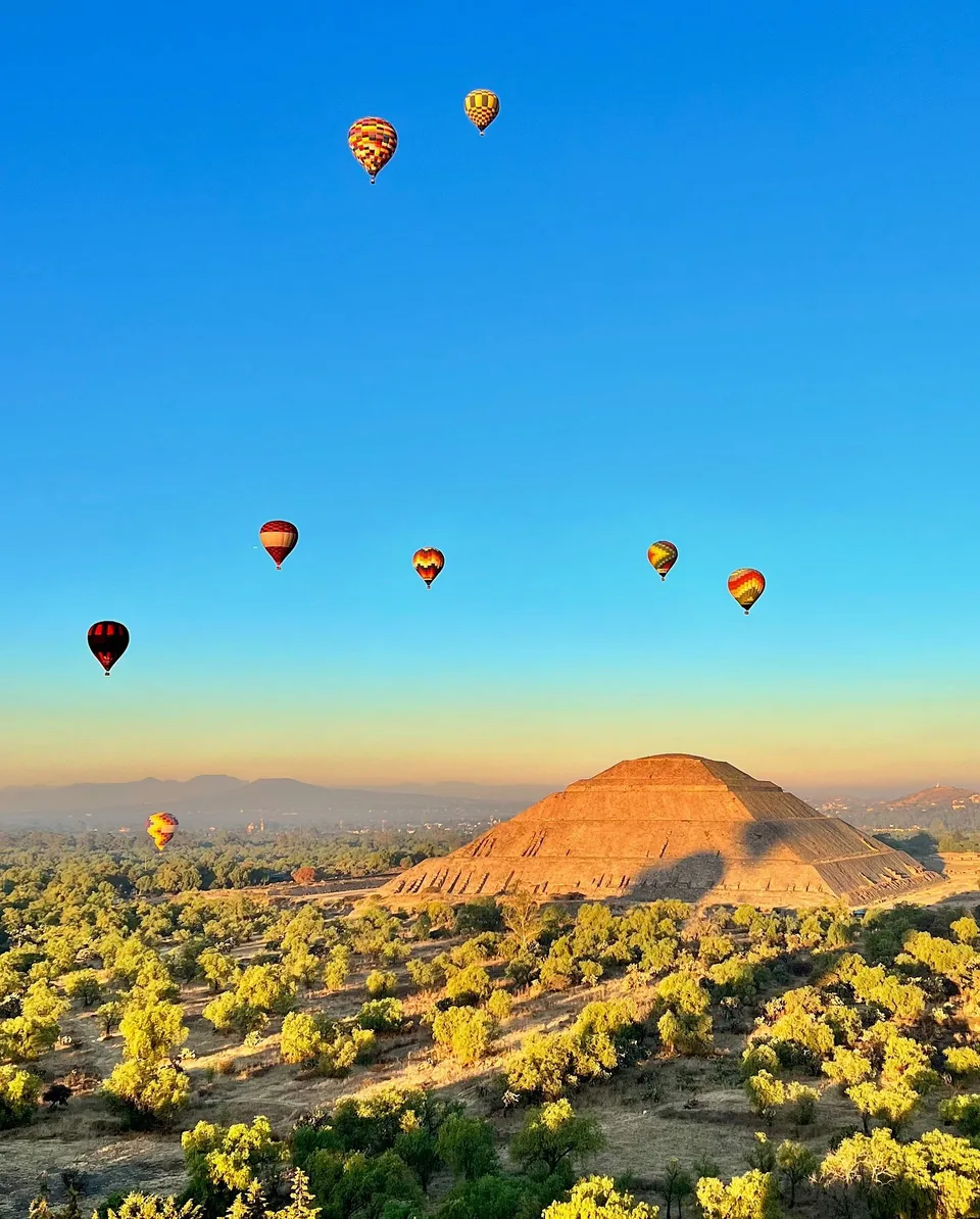 Hot air balloons above the Pyramid of the Sun against a deep blue sky