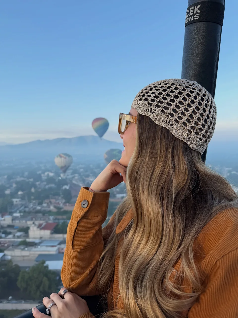 A passenger resting both arms on the padded rail of a hot air balloon basket over the Teotihuacan valley