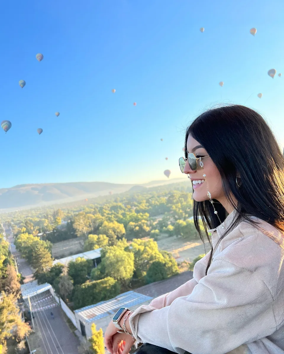 A smiling passenger in flight with the Teotihuacan valley and distant balloons behind