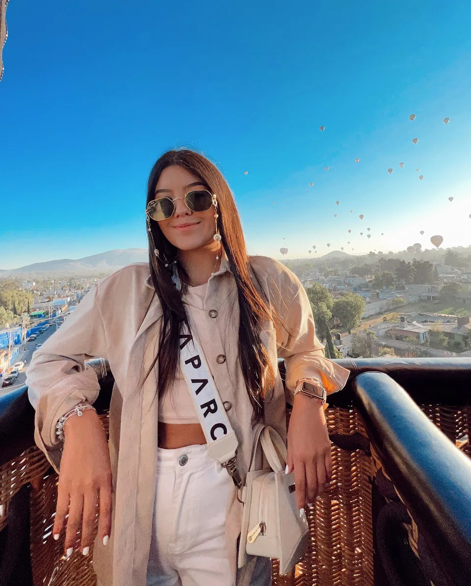 An adult passenger standing in a hot air balloon basket over the Teotihuacan valley, the basket wall reaching chest height