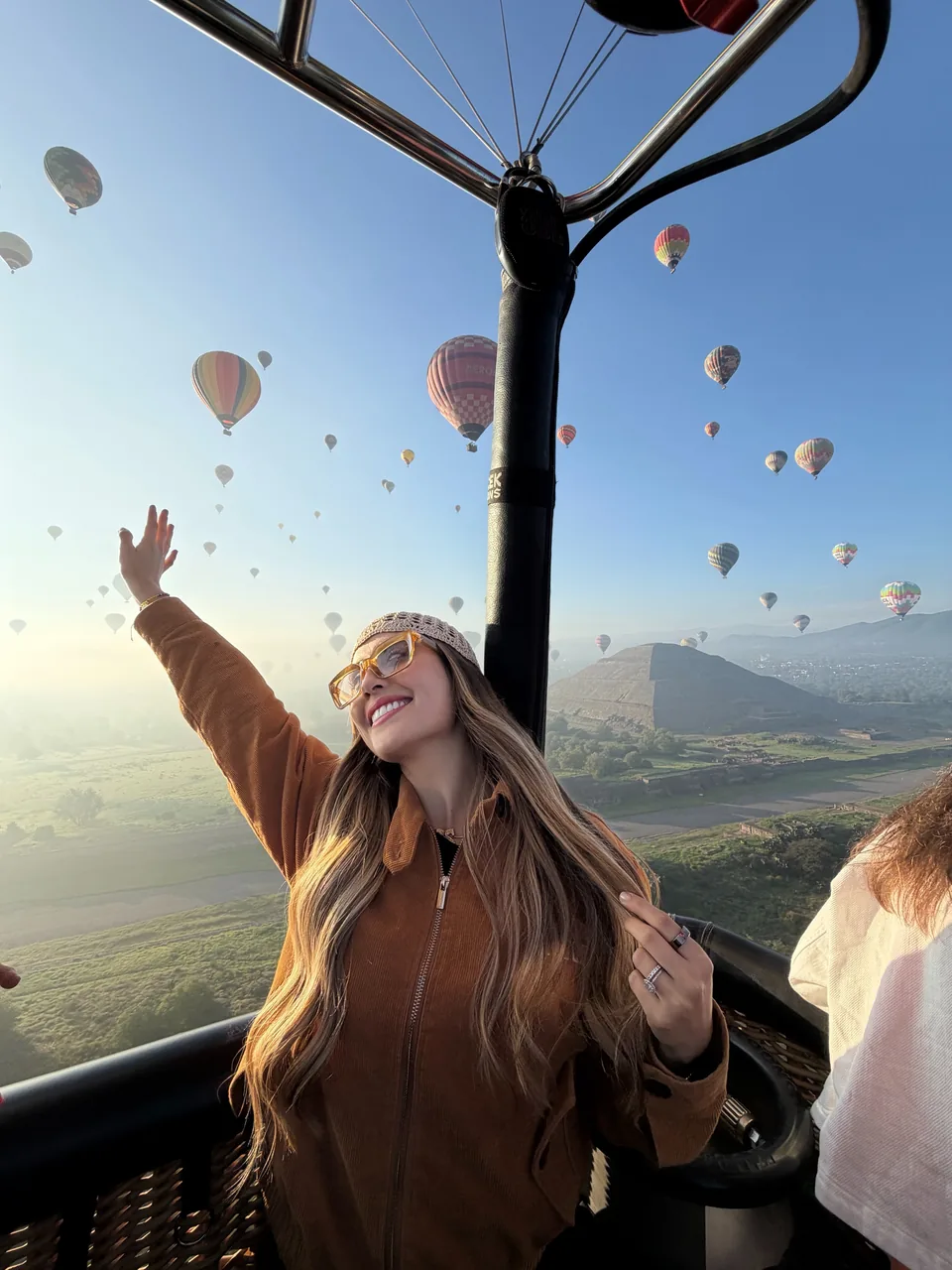 A passenger raises an arm in the basket as balloons and the Pyramid of the Sun fill the view