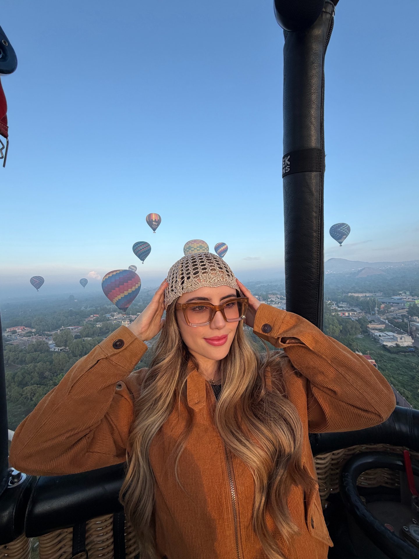 A passenger stands at the basket edge with the Teotihuacan valley and dozens of balloons behind
